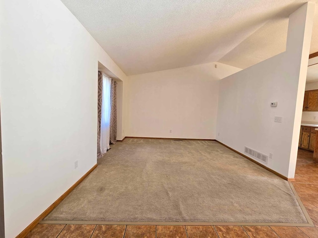 tiled empty room featuring a textured ceiling and lofted ceiling