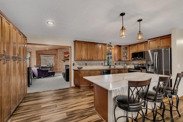 kitchen with light stone counters, stainless steel appliances, sink, pendant lighting, and a center island