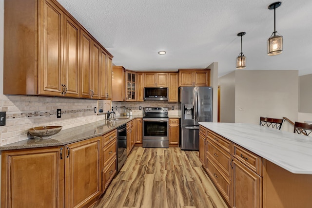 kitchen featuring appliances with stainless steel finishes, light stone counters, pendant lighting, light hardwood / wood-style floors, and a breakfast bar area