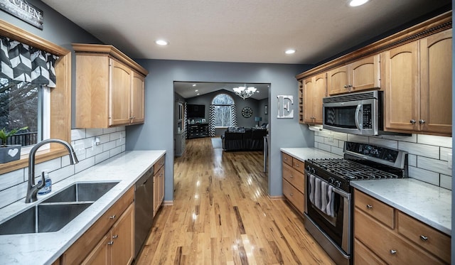 kitchen with backsplash, stainless steel appliances, sink, light hardwood / wood-style flooring, and a notable chandelier