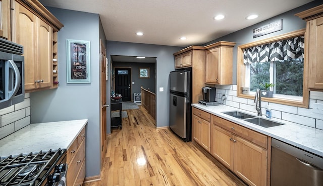 kitchen featuring decorative backsplash, light wood-type flooring, light stone counters, stainless steel appliances, and sink