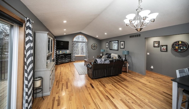 living room with a chandelier, a textured ceiling, light hardwood / wood-style floors, and vaulted ceiling