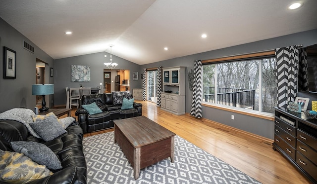 living room featuring light wood-type flooring, an inviting chandelier, and lofted ceiling