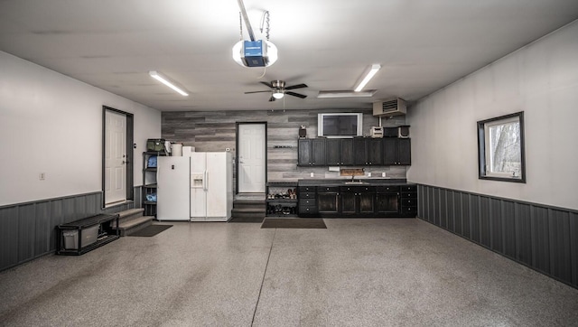 garage with ceiling fan, white fridge with ice dispenser, sink, and a garage door opener