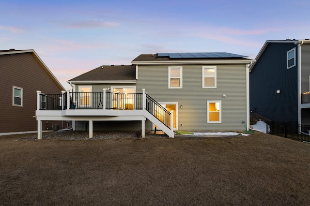 back house at dusk featuring a yard, a deck, and solar panels