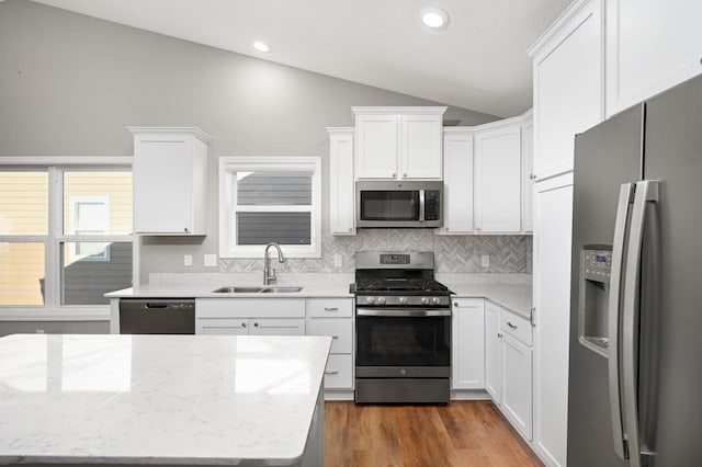 kitchen featuring sink, stainless steel appliances, light stone counters, white cabinets, and vaulted ceiling