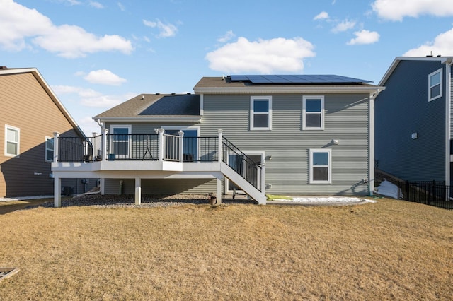 rear view of house with a wooden deck, a yard, and solar panels