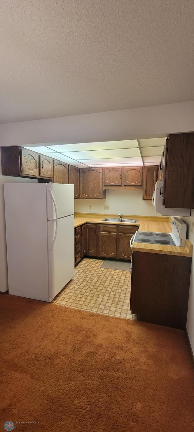 kitchen featuring a textured ceiling, sink, white appliances, and light carpet