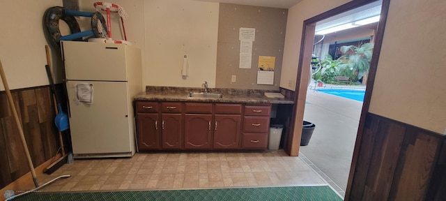 kitchen featuring white refrigerator, sink, and wooden walls