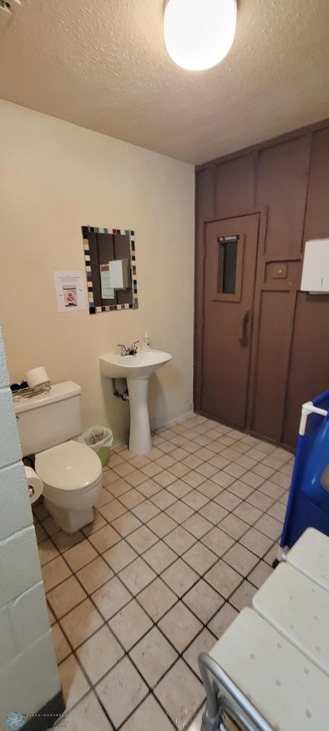 bathroom with toilet, sink, a textured ceiling, and tile patterned flooring