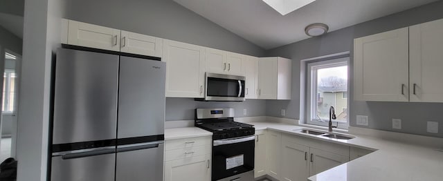 kitchen with appliances with stainless steel finishes, white cabinetry, lofted ceiling, and sink