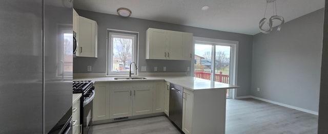 kitchen with stainless steel appliances, a peninsula, a sink, light countertops, and light wood finished floors