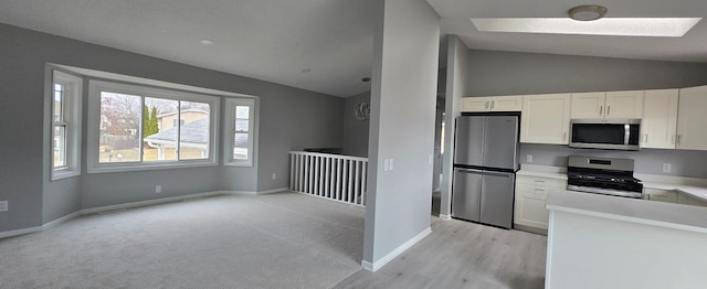 kitchen featuring vaulted ceiling, stainless steel appliances, light carpet, and white cabinetry