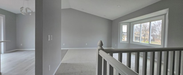 corridor with vaulted ceiling, light colored carpet, an upstairs landing, and baseboards