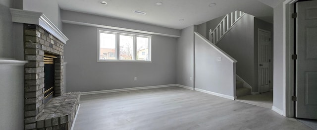 unfurnished living room featuring stairway, a brick fireplace, wood finished floors, and visible vents