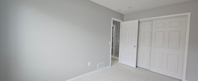 unfurnished bedroom featuring light colored carpet, a closet, visible vents, and baseboards