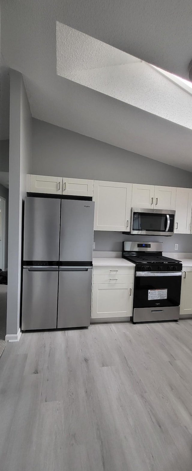 kitchen with stainless steel appliances, white cabinets, vaulted ceiling, and light wood finished floors