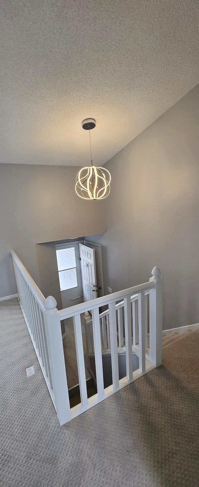 staircase featuring a chandelier, a textured ceiling, and carpet flooring