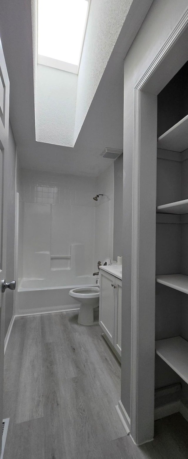 bathroom with a skylight, toilet, vanity, shower / tub combination, and wood finished floors