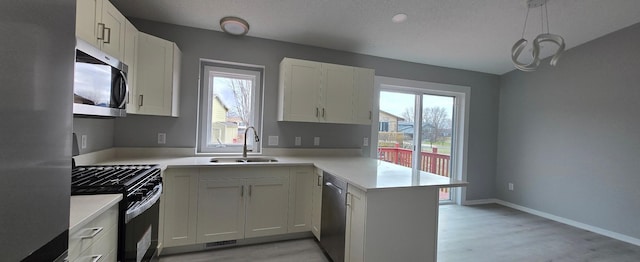 kitchen with light countertops, appliances with stainless steel finishes, a sink, a peninsula, and baseboards