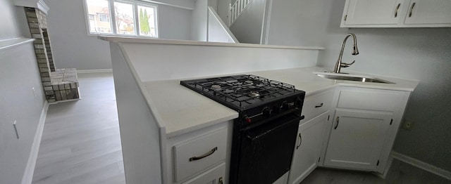 kitchen with light wood-style flooring, a sink, white cabinetry, light countertops, and black range with gas stovetop