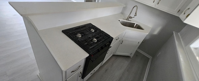 kitchen featuring black range with gas cooktop, light wood-style flooring, light countertops, white cabinetry, and a sink