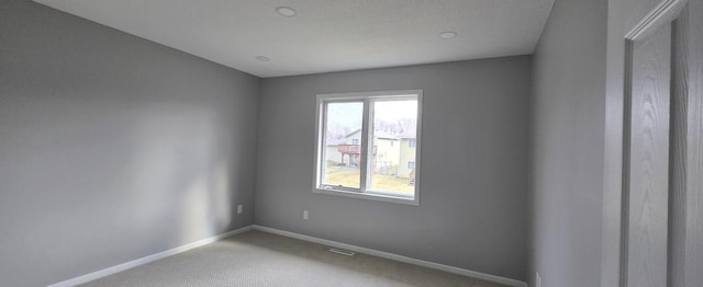 carpeted spare room with visible vents and baseboards