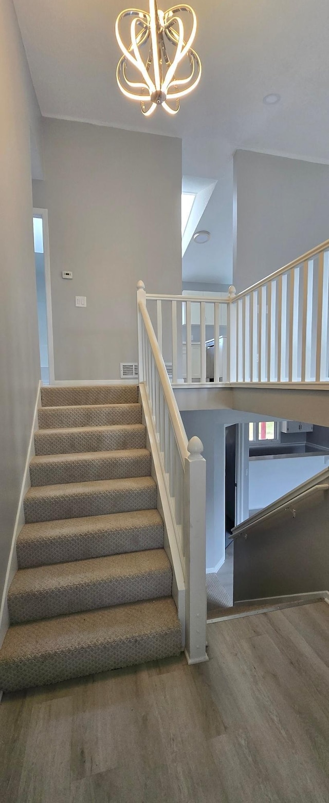 staircase with baseboards, visible vents, wood finished floors, a high ceiling, and a notable chandelier