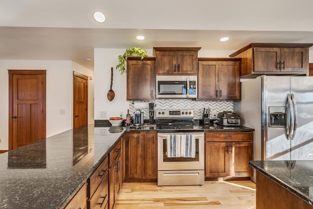 kitchen featuring appliances with stainless steel finishes, light hardwood / wood-style floors, tasteful backsplash, and dark stone countertops