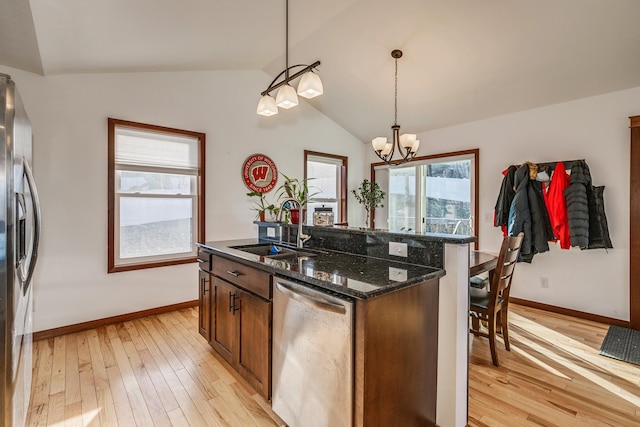 kitchen with light wood-type flooring, dark stone counters, stainless steel appliances, sink, and decorative light fixtures