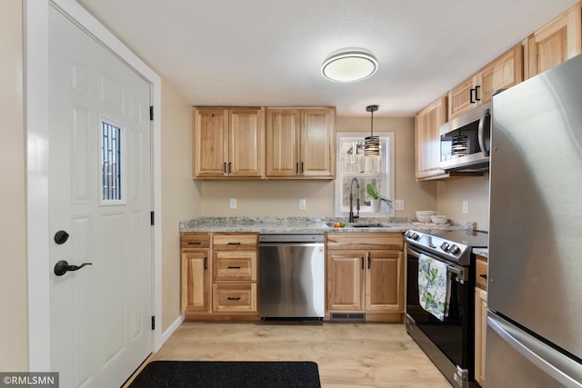 kitchen with decorative light fixtures, sink, light stone counters, light hardwood / wood-style floors, and stainless steel appliances