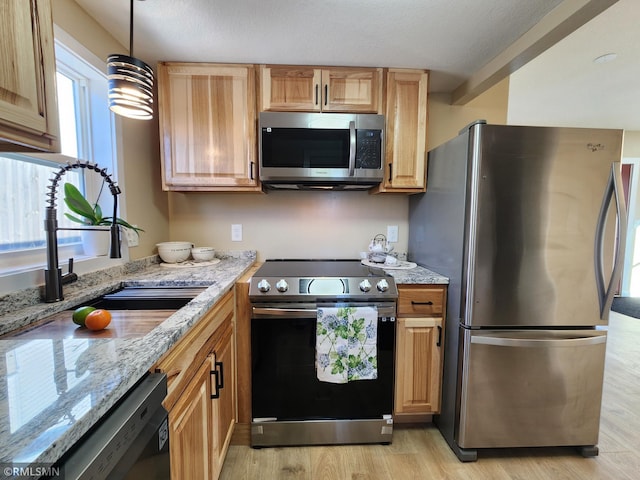 kitchen featuring sink, hanging light fixtures, light hardwood / wood-style flooring, appliances with stainless steel finishes, and light stone countertops