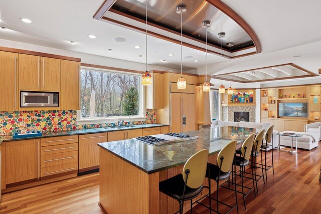 kitchen with built in appliances, light wood-style floors, open floor plan, a kitchen bar, and a tray ceiling