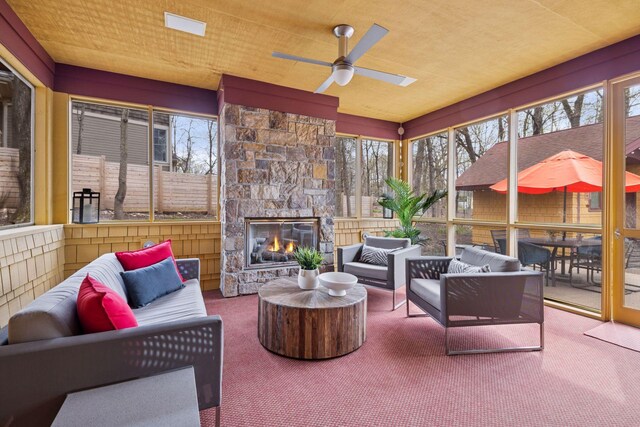 sunroom featuring carpet flooring, an outdoor living space with a fireplace, and a ceiling fan