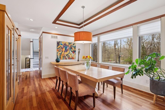 dining room with baseboards, a tray ceiling, visible vents, and wood finished floors