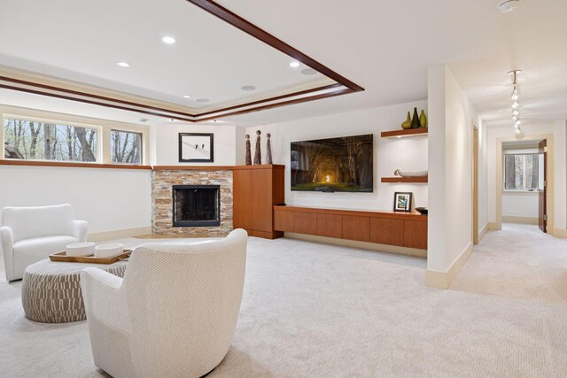 living room with a stone fireplace, light colored carpet, baseboards, a tray ceiling, and recessed lighting