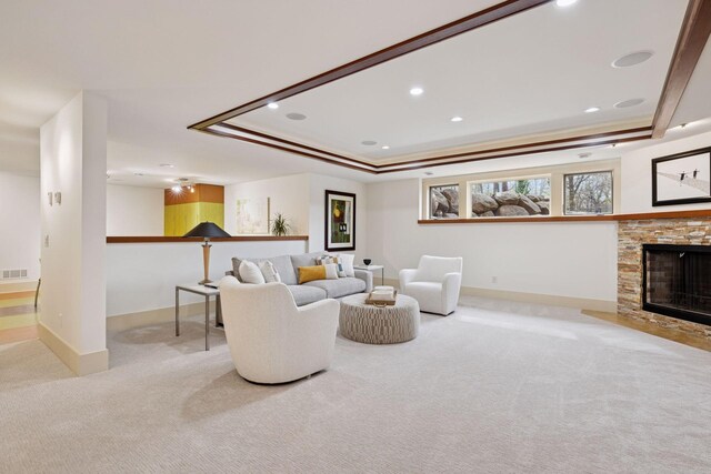 carpeted living area featuring baseboards, a raised ceiling, visible vents, and a fireplace