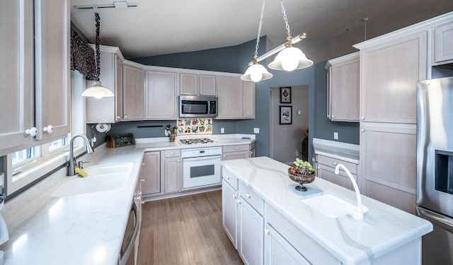 kitchen featuring sink, hardwood / wood-style floors, vaulted ceiling, decorative light fixtures, and appliances with stainless steel finishes