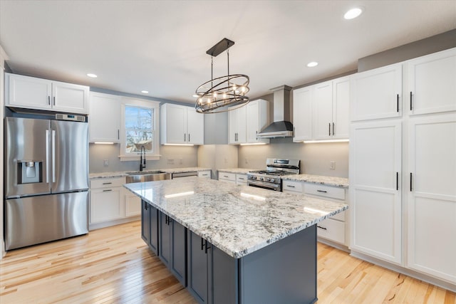 kitchen with pendant lighting, appliances with stainless steel finishes, white cabinetry, a sink, and wall chimney range hood