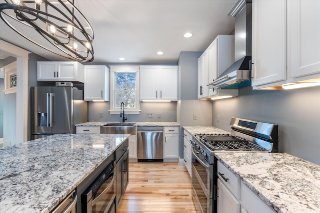 kitchen featuring stainless steel appliances, white cabinetry, hanging light fixtures, and wall chimney exhaust hood