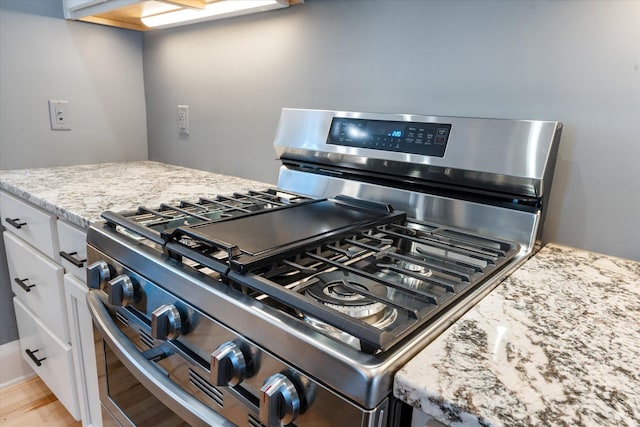 kitchen featuring light stone countertops, light wood-style flooring, white cabinets, and stainless steel range with gas stovetop