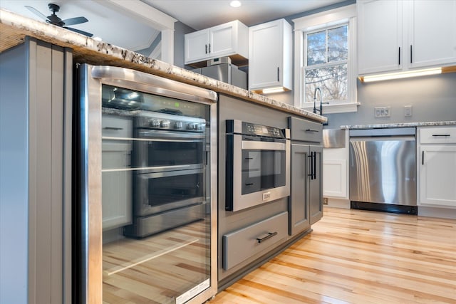 kitchen featuring light wood finished floors, light stone counters, stainless steel dishwasher, and white cabinetry