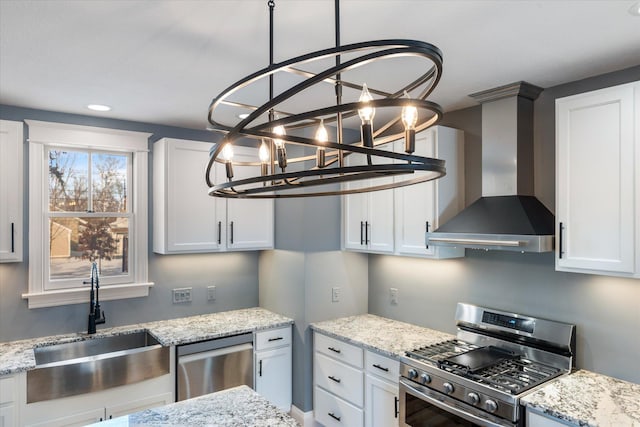 kitchen featuring stainless steel appliances, wall chimney range hood, a sink, and white cabinetry