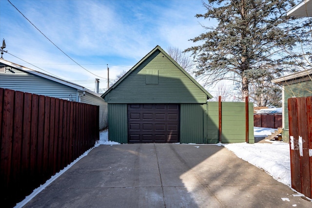 snow covered garage featuring a garage, concrete driveway, and fence