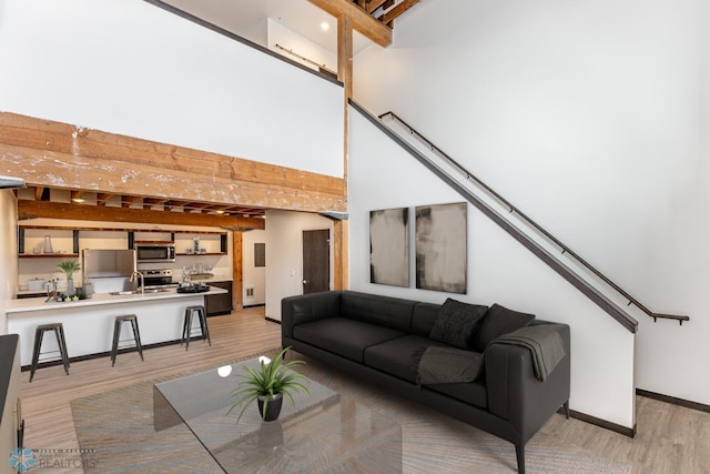 living room with beam ceiling, sink, and light hardwood / wood-style flooring