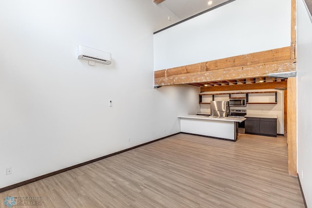 kitchen featuring beam ceiling, kitchen peninsula, light wood-type flooring, and appliances with stainless steel finishes