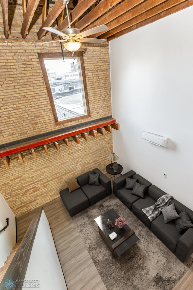 unfurnished living room with hardwood / wood-style flooring, ceiling fan, beam ceiling, and brick wall