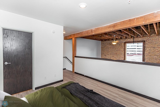 unfurnished bedroom with brick wall, wood finished floors, baseboards, a closet, and beam ceiling