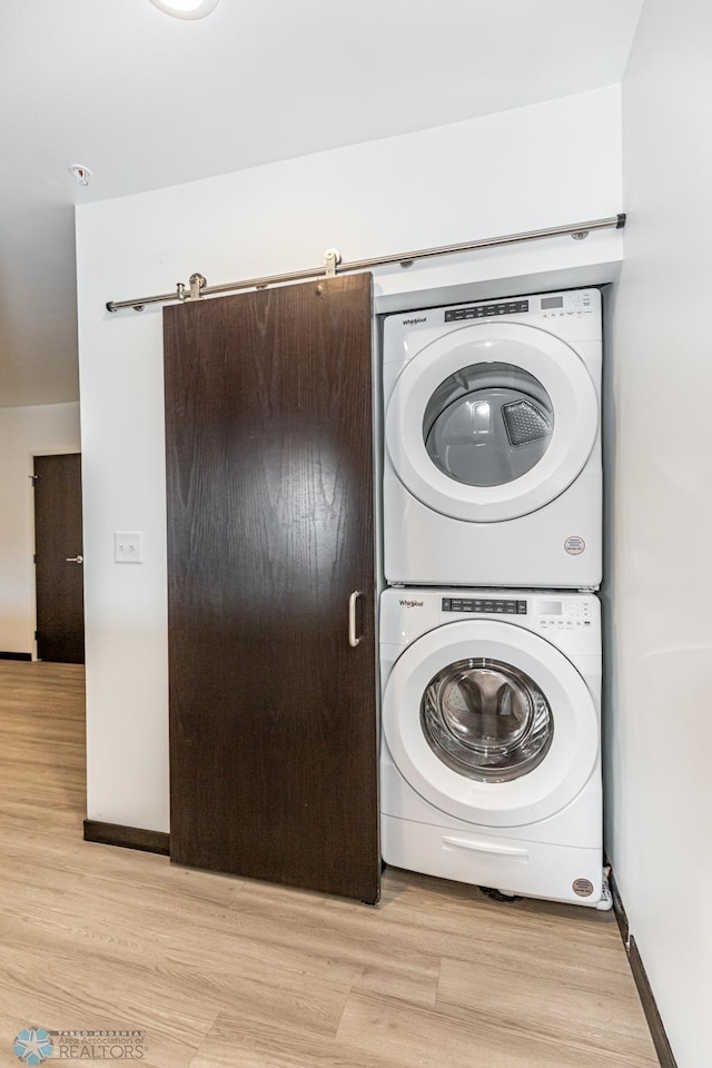 laundry room featuring stacked washing maching and dryer and light hardwood / wood-style floors