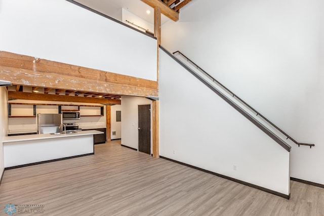 kitchen with a peninsula, a sink, baseboards, appliances with stainless steel finishes, and light wood finished floors